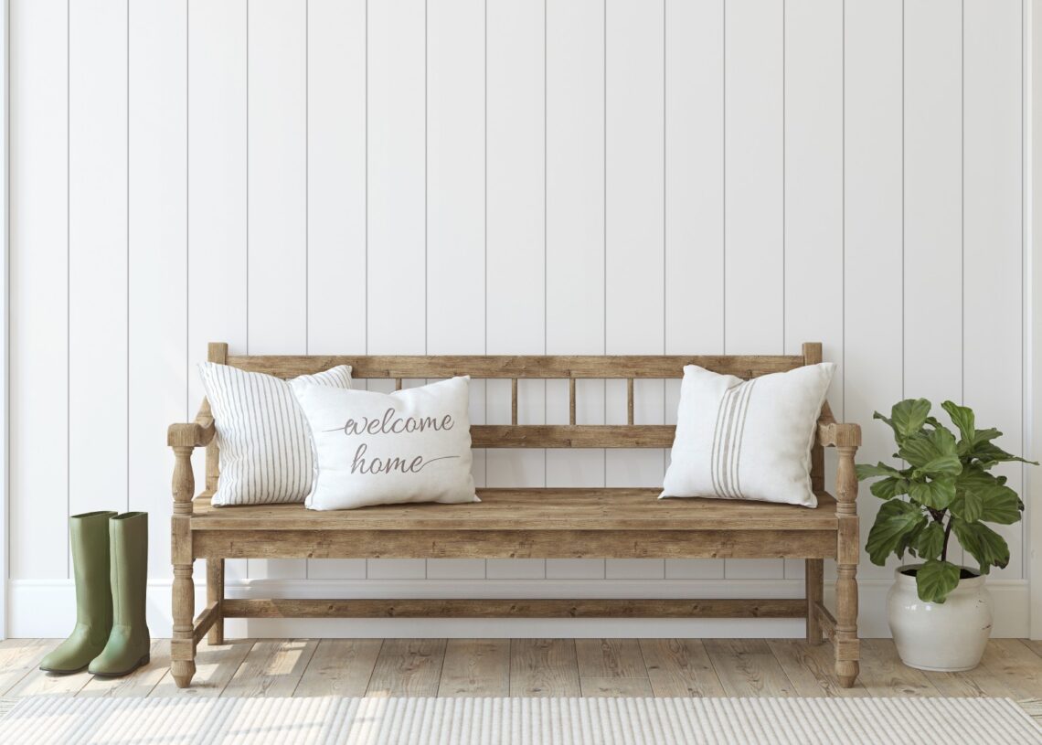 A wooden bench with white decorative pillows sits in front of a white wall in the inviting entryway of a mobile home.