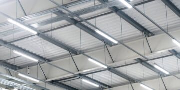 Close-up of six rows of high-bay LED lighting in a warehouse installed on silver beams against a white ceiling.