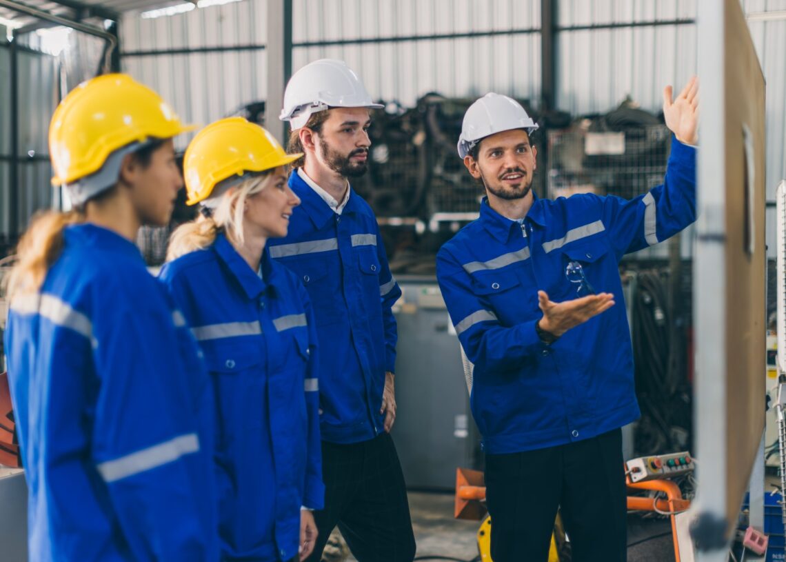 A construction manager trains his workers with the help of a white board. They all wear blue jackets.