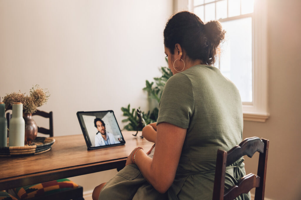 A woman wearing a green shirt is holding a baby while having a telemedicine appointment with a doctor.
