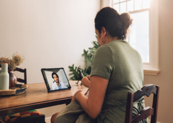 A woman wearing a green shirt is holding a baby while having a telemedicine appointment with a doctor.