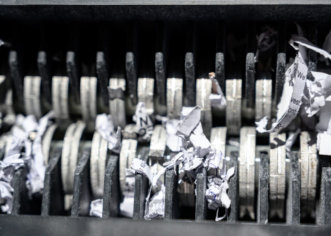 An extreme close-up view shows the metal teeth of a shredder. The teeth are shredding white paper.