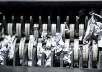 An extreme close-up view shows the metal teeth of a shredder. The teeth are shredding white paper.