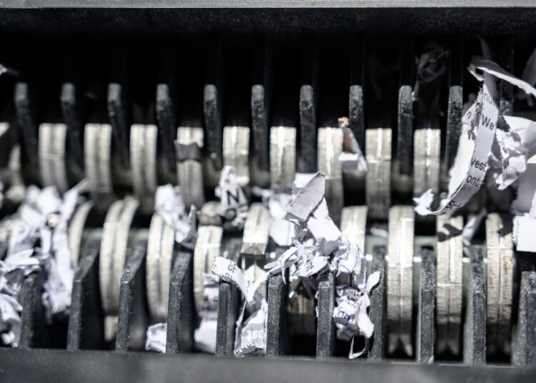 An extreme close-up view shows the metal teeth of a shredder. The teeth are shredding white paper.