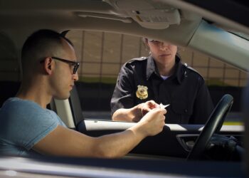 A man sitting in a vehicle is handing over an ID card to a female police officer standing by his window.