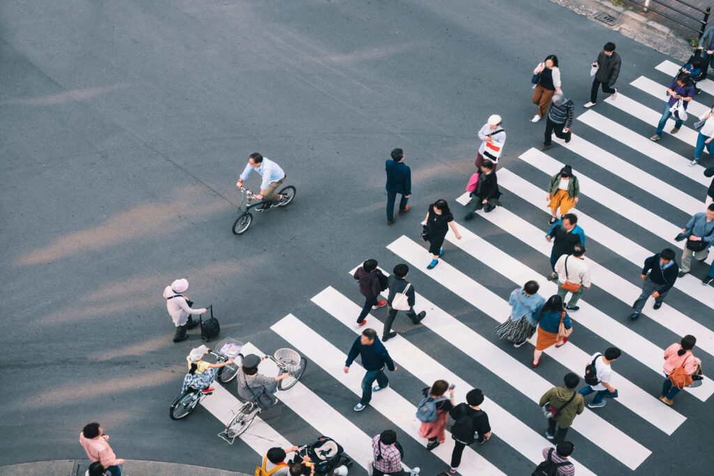 An aerial view shows several people walking across a crosswalk on a road. Some people are riding bikes.