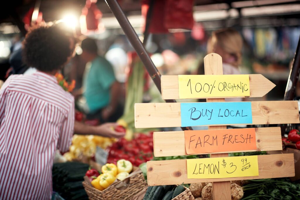 A wooden sign contains handwritten notes that read “100% organic, buy local, farm fresh, lemons $3.99.”