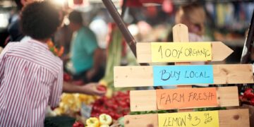 A wooden sign contains handwritten notes that read “100% organic, buy local, farm fresh, lemons $3.99.”