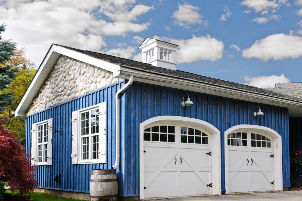 A two-car garage with bright blue siding. It also has white, barnyard style doors with windowpanes and black hardware.