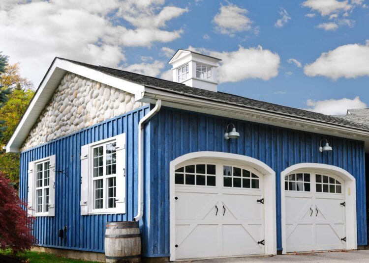 A two-car garage with bright blue siding. It also has white, barnyard style doors with windowpanes and black hardware.