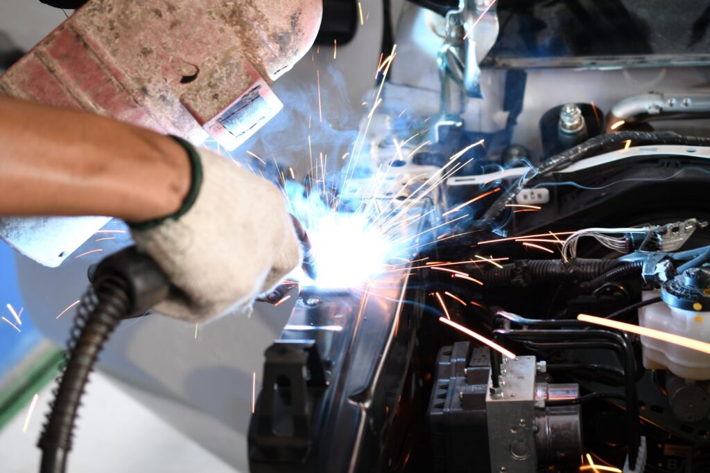 A close-up of a male welder welding an automotive part in an auto body repair shop. Sparks are flying.