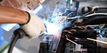 A close-up of a male welder welding an automotive part in an auto body repair shop. Sparks are flying.