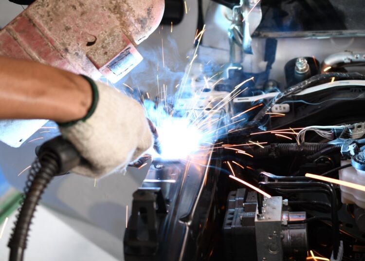 A close-up of a male welder welding an automotive part in an auto body repair shop. Sparks are flying.