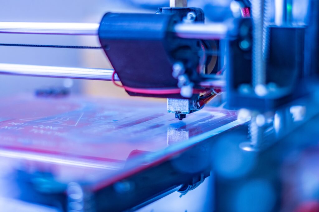 A close-up of a machine manufacturing something with precision. There are pink, blue, and purple neon lights.