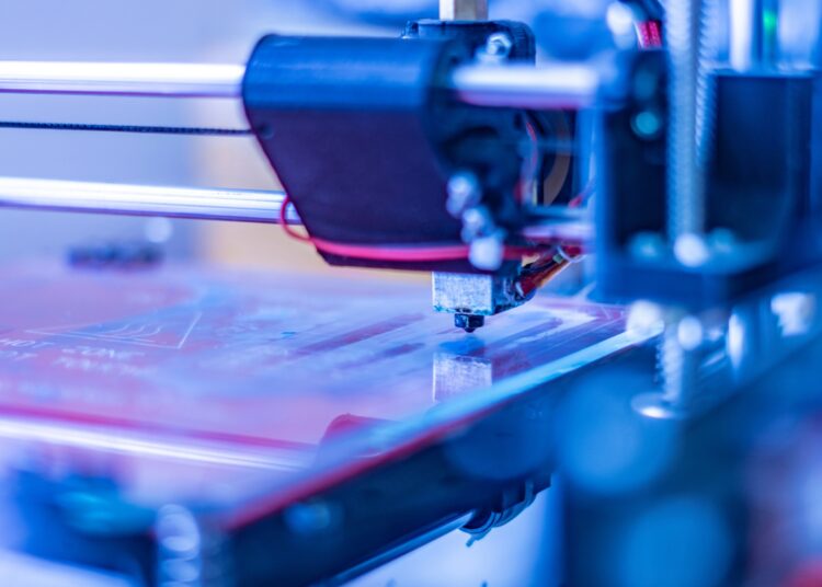 A close-up of a machine manufacturing something with precision. There are pink, blue, and purple neon lights.