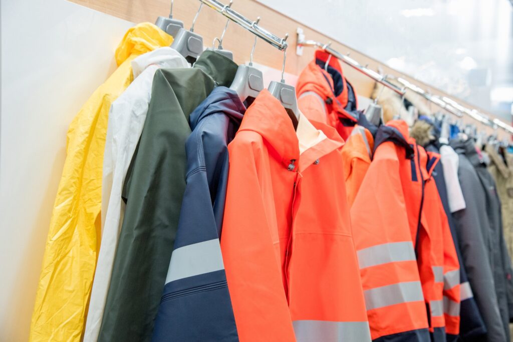 Different blue-collar workplace safety clothing tops hang on a metal rack inside a brightly-lit store.