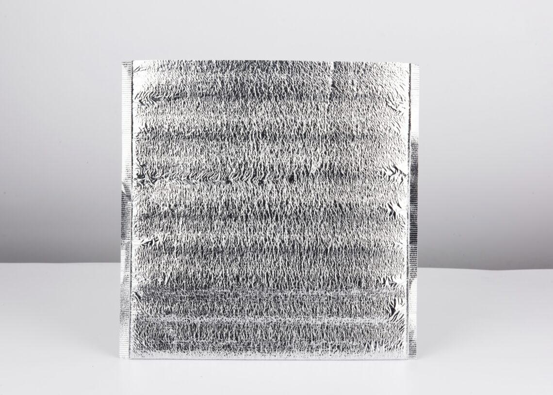 A silver thermal pouch sits alone on a white and gray background. The top of the bag is cut open.