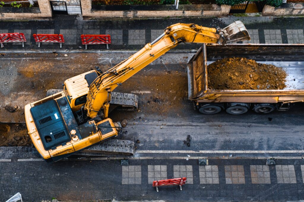 An overview of a big yellow forklift lifting the ground to make room for new infrastructure outside of a building.