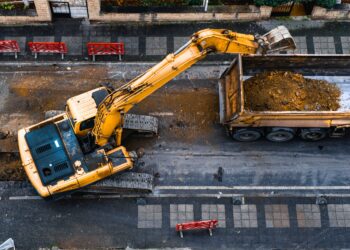 An overview of a big yellow forklift lifting the ground to make room for new infrastructure outside of a building.