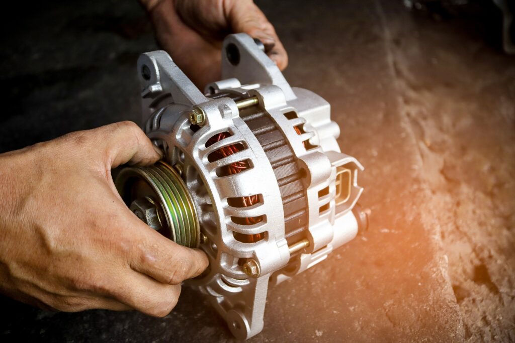 A person holding a brand-new car alternator with both hands. Copper wiring is visible within the alternator.