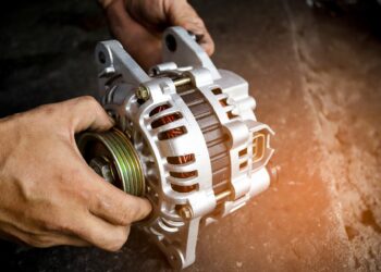 A person holding a brand-new car alternator with both hands. Copper wiring is visible within the alternator.