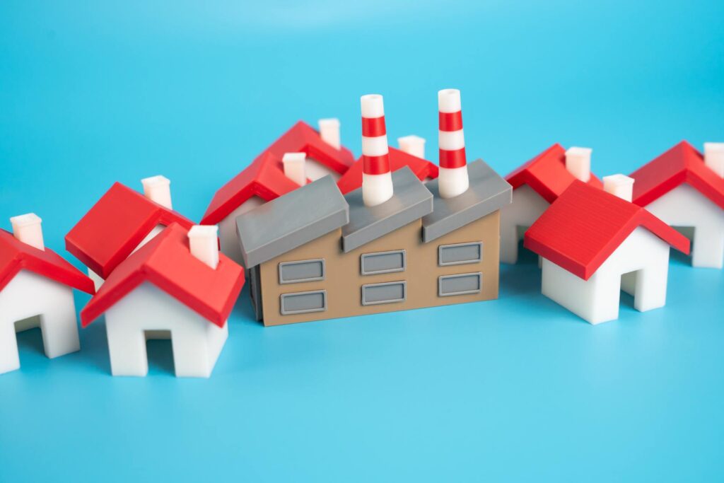 A bunch of tiny model homes crowded around an industrial building model. All of these are sitting against a blue backdrop.