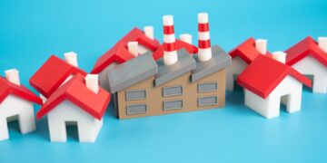 A bunch of tiny model homes crowded around an industrial building model. All of these are sitting against a blue backdrop.