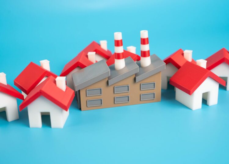 A bunch of tiny model homes crowded around an industrial building model. All of these are sitting against a blue backdrop.