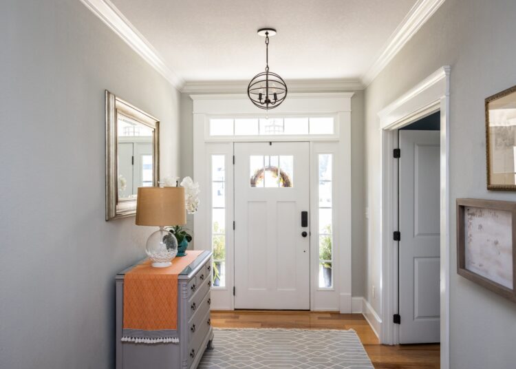 An entrance to a residential home. There is a white door with windows showing light coming in from outside.