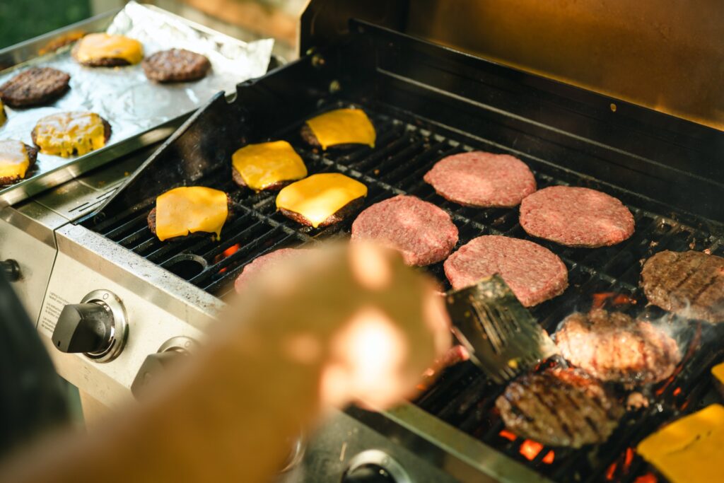 There are many burger patties on a grill. Some are cooked while others still look raw. Some have cheese on them.
