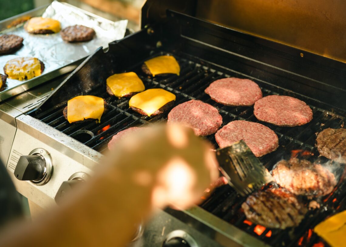 There are many burger patties on a grill. Some are cooked while others still look raw. Some have cheese on them.