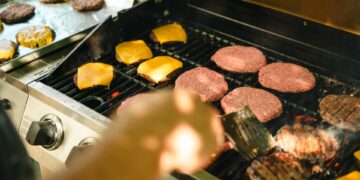 There are many burger patties on a grill. Some are cooked while others still look raw. Some have cheese on them.