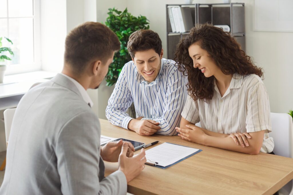 Three people are at a desk; a man and a woman are on one side while another man is sitting across from them.