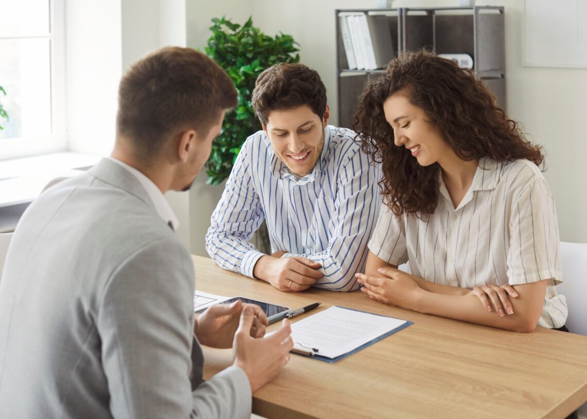 Three people are at a desk; a man and a woman are on one side while another man is sitting across from them.