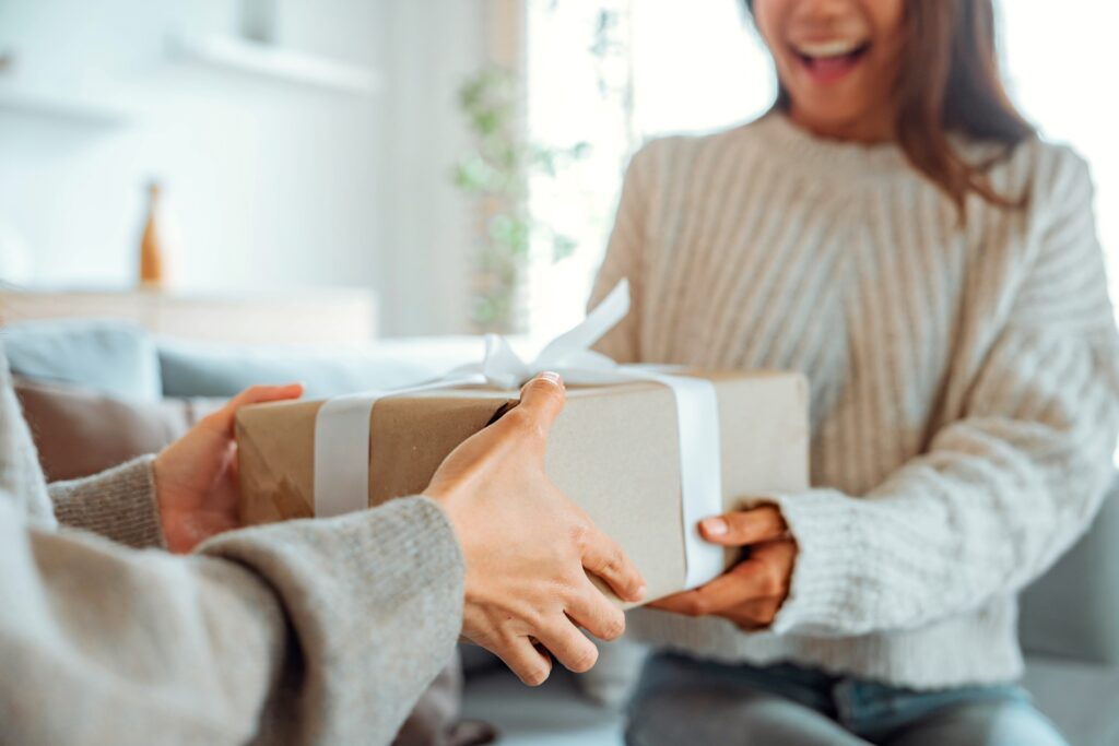 A smiling woman is holding a wrapped present in her hands as someone gives it to her.