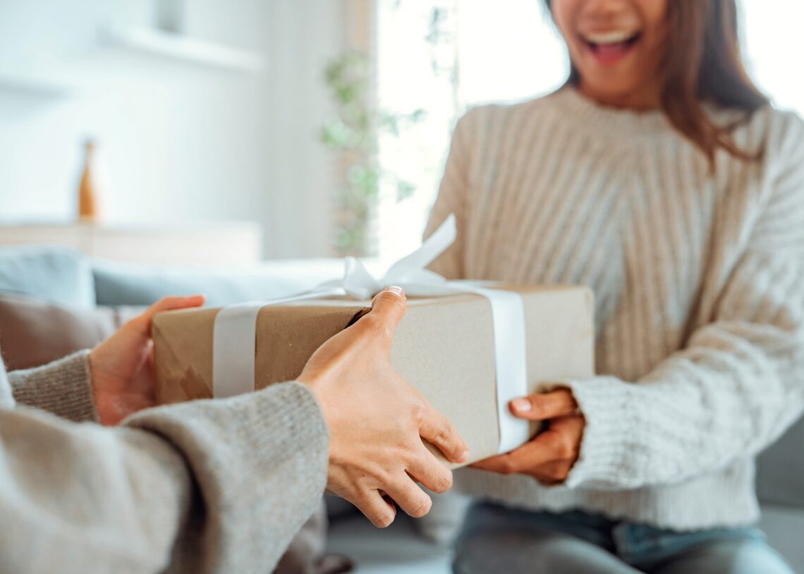 A smiling woman is holding a wrapped present in her hands as someone gives it to her.