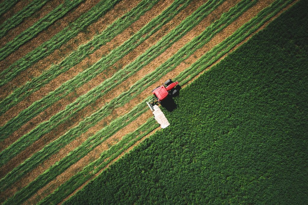 An overhead view of a tractor plowing a section of farmland. The tractor has made rows in half of the field.