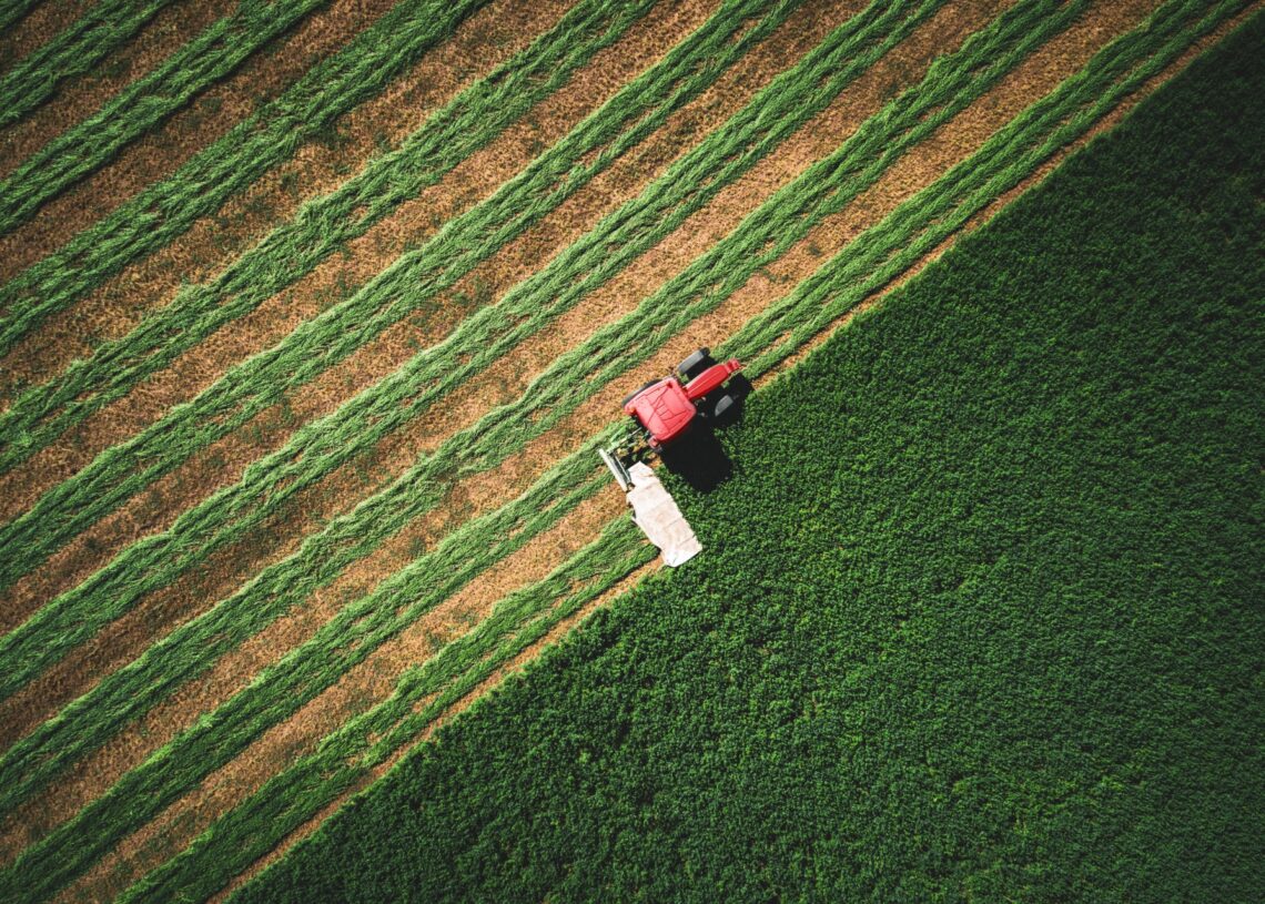 An overhead view of a tractor plowing a section of farmland. The tractor has made rows in half of the field.