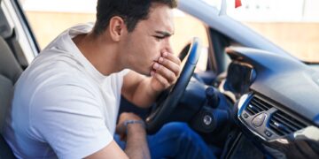 A man is sitting in the driver’s seat of a car as he is examining the air vents on the dashboard.