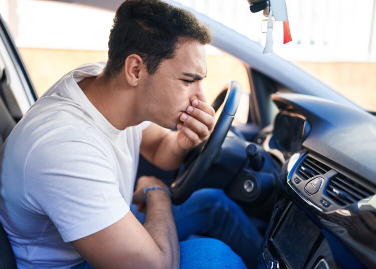 A man is sitting in the driver’s seat of a car as he is examining the air vents on the dashboard.
