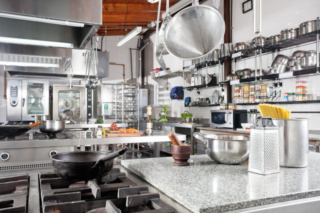 A professional commercial kitchen with stainless steel equipment, organized shelving, and cooking stations for food preparation.