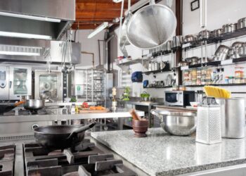 A professional commercial kitchen with stainless steel equipment, organized shelving, and cooking stations for food preparation.