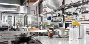 A professional commercial kitchen with stainless steel equipment, organized shelving, and cooking stations for food preparation.
