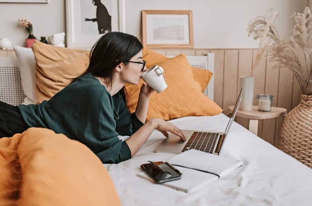 A woman lying on her bed while looking at her laptop