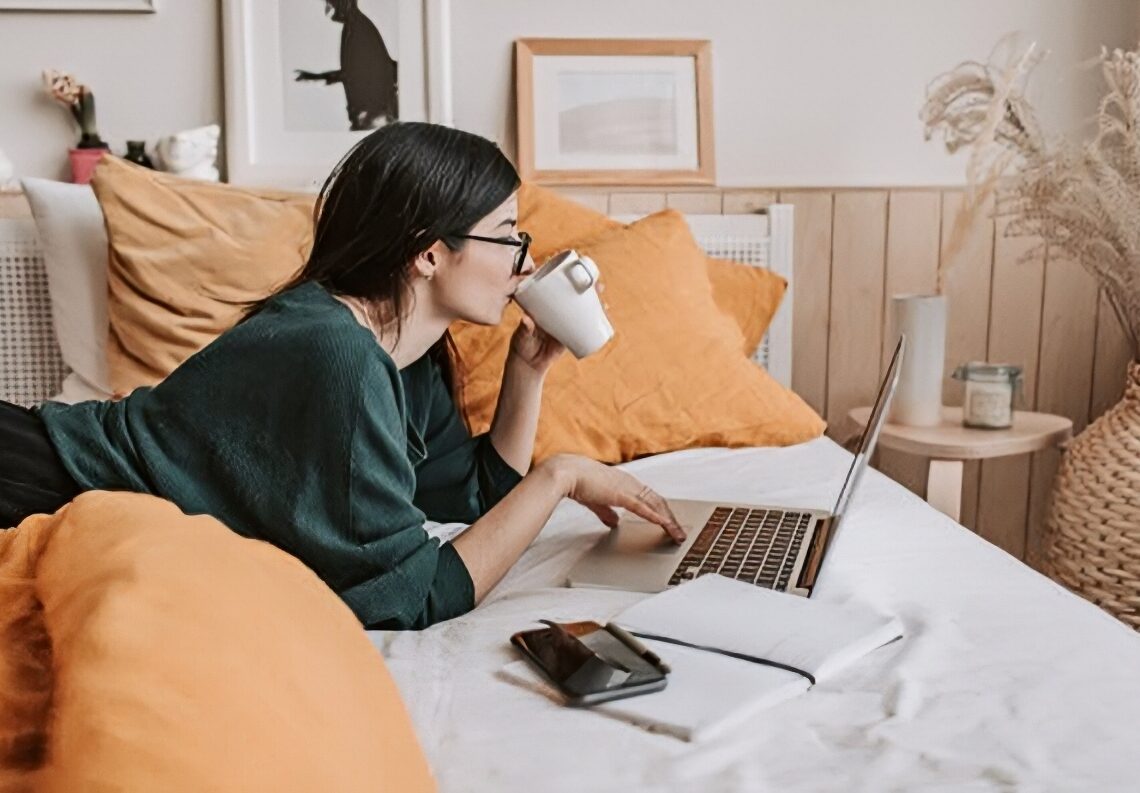A woman lying on her bed while looking at her laptop