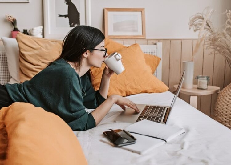A woman lying on her bed while looking at her laptop