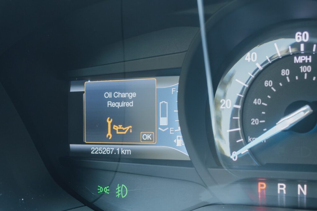 A car dashboard showing an illuminated “Oil Change Required” warning with a wrench icon next to the speedometer.