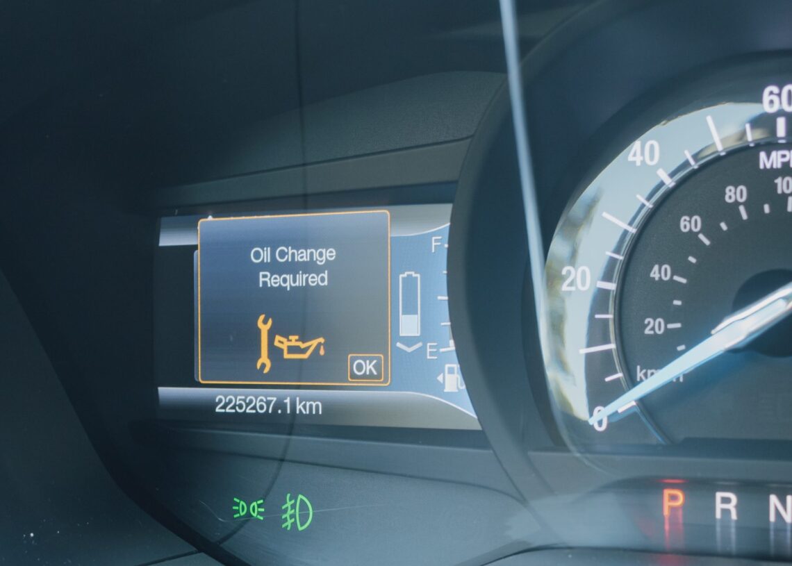 A car dashboard showing an illuminated “Oil Change Required” warning with a wrench icon next to the speedometer.