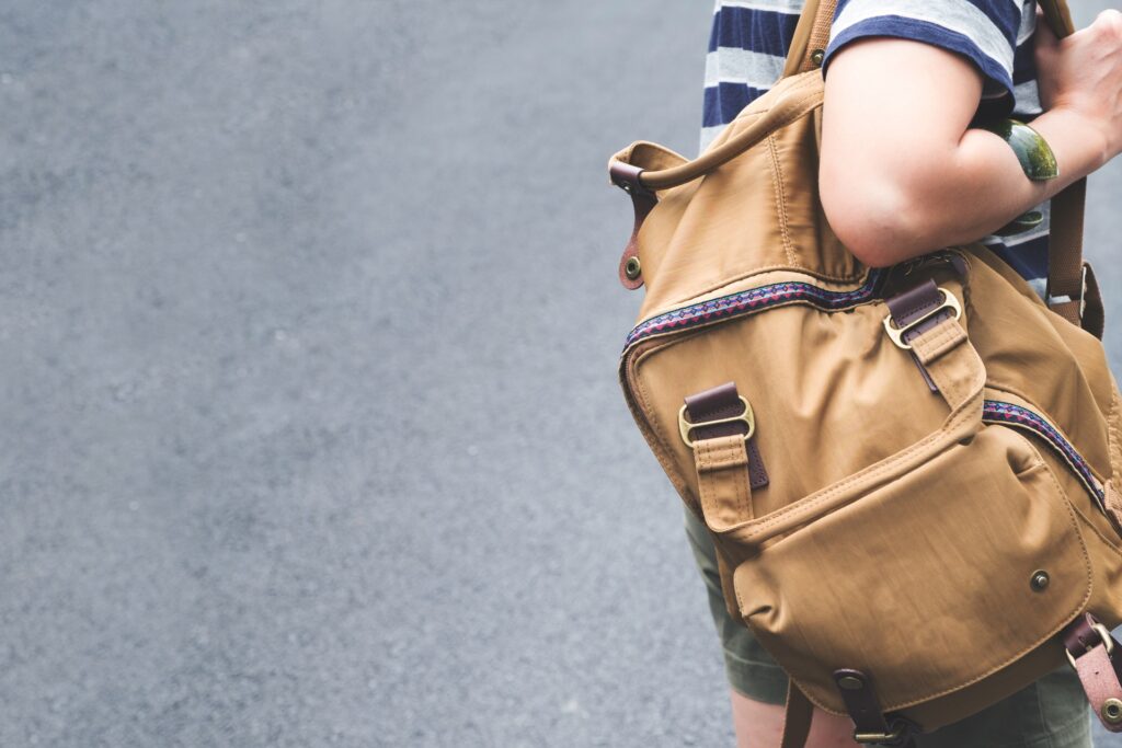 A person in a striped shirt shown from behind carrying a large backpack while walking along a paved street outdoors.