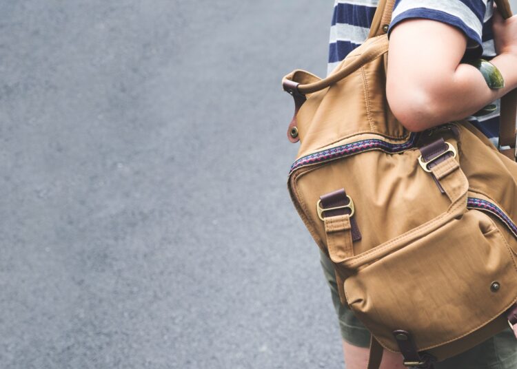 A person in a striped shirt shown from behind carrying a large backpack while walking along a paved street outdoors.